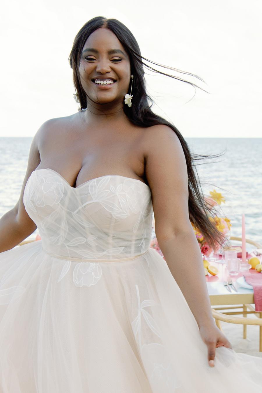 Custom-designed floral motifs dance their way across the structured bodice and trickle down the skirt of this romantic ballgown. Dotted netting sewn into the skirt provides additional dimension, while layers upon layers of tulle melt together to create a soft oatmeal shade to highlight the oversized motifs.