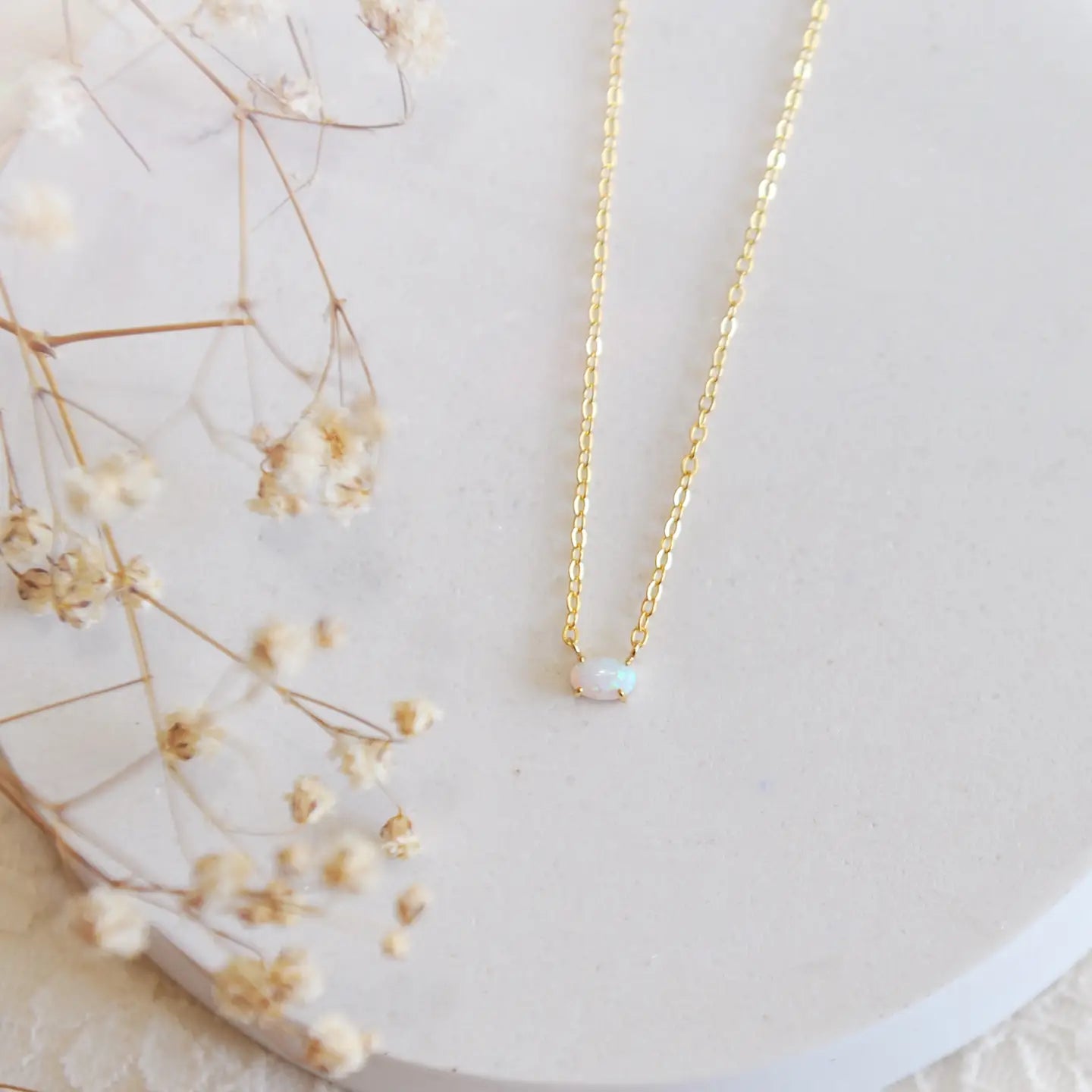 A white opal on a gold dainty chain on a white background
