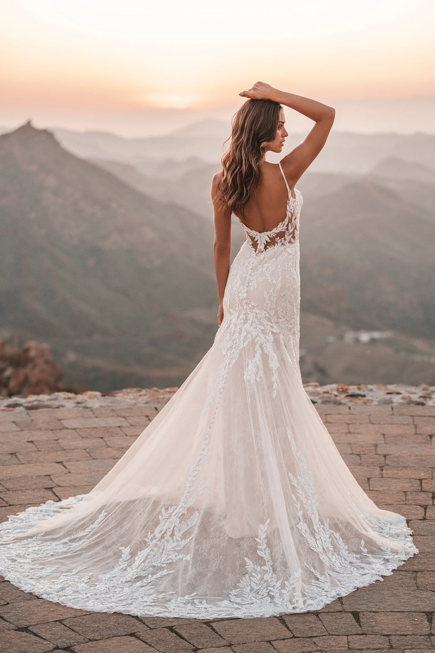 Woman in a white lace dress standing on a stone path with mountains in the background