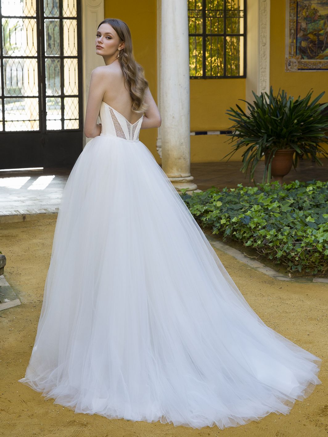 Woman in a white wedding dress standing in an outdoor setting with columns and plants.