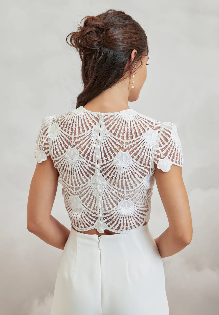 Woman wearing a white lace top against a plain background