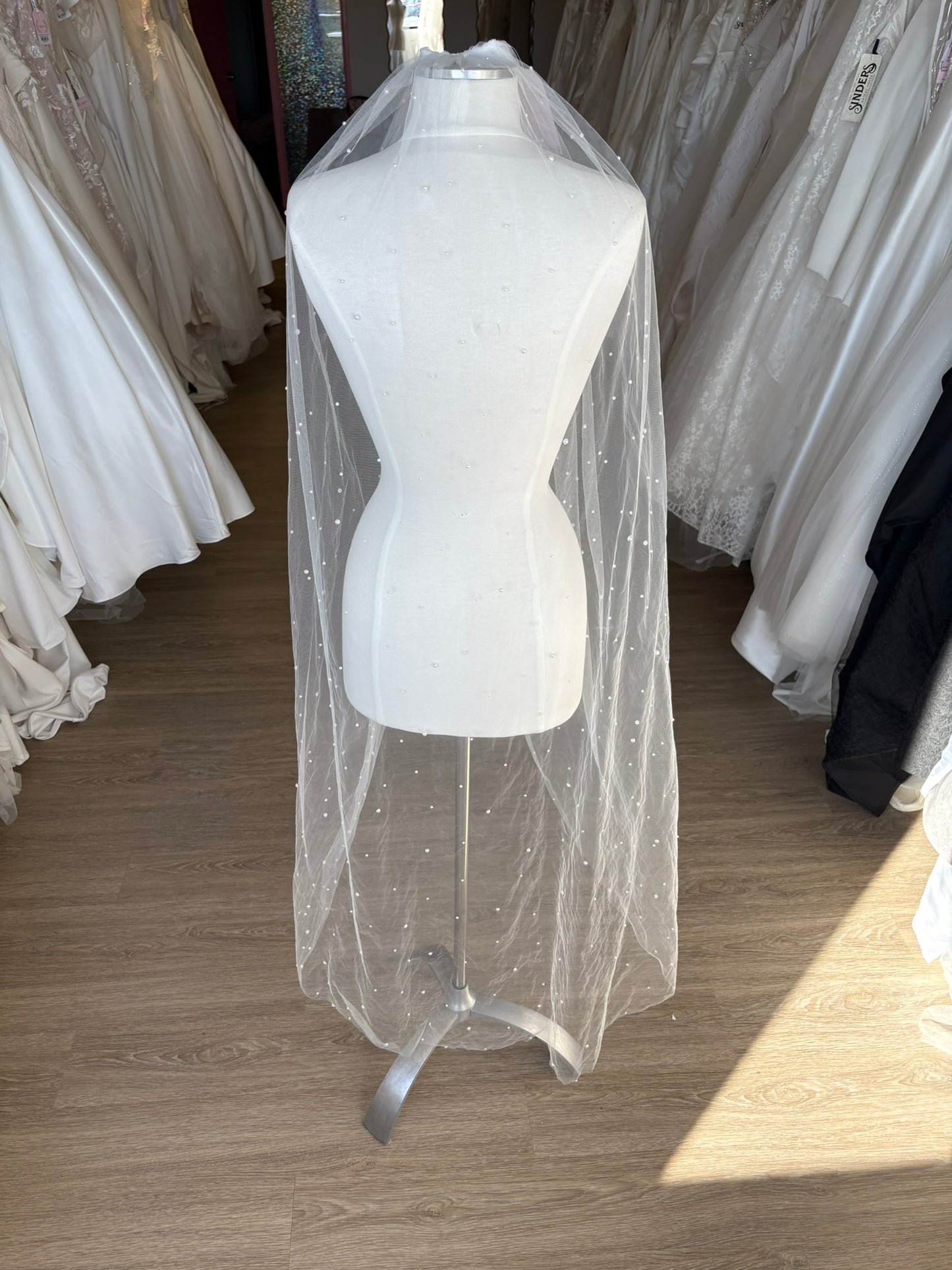 White wedding veil knee length with flat back ivory pearl on a mannequin in a store setting with other wedding dresses.