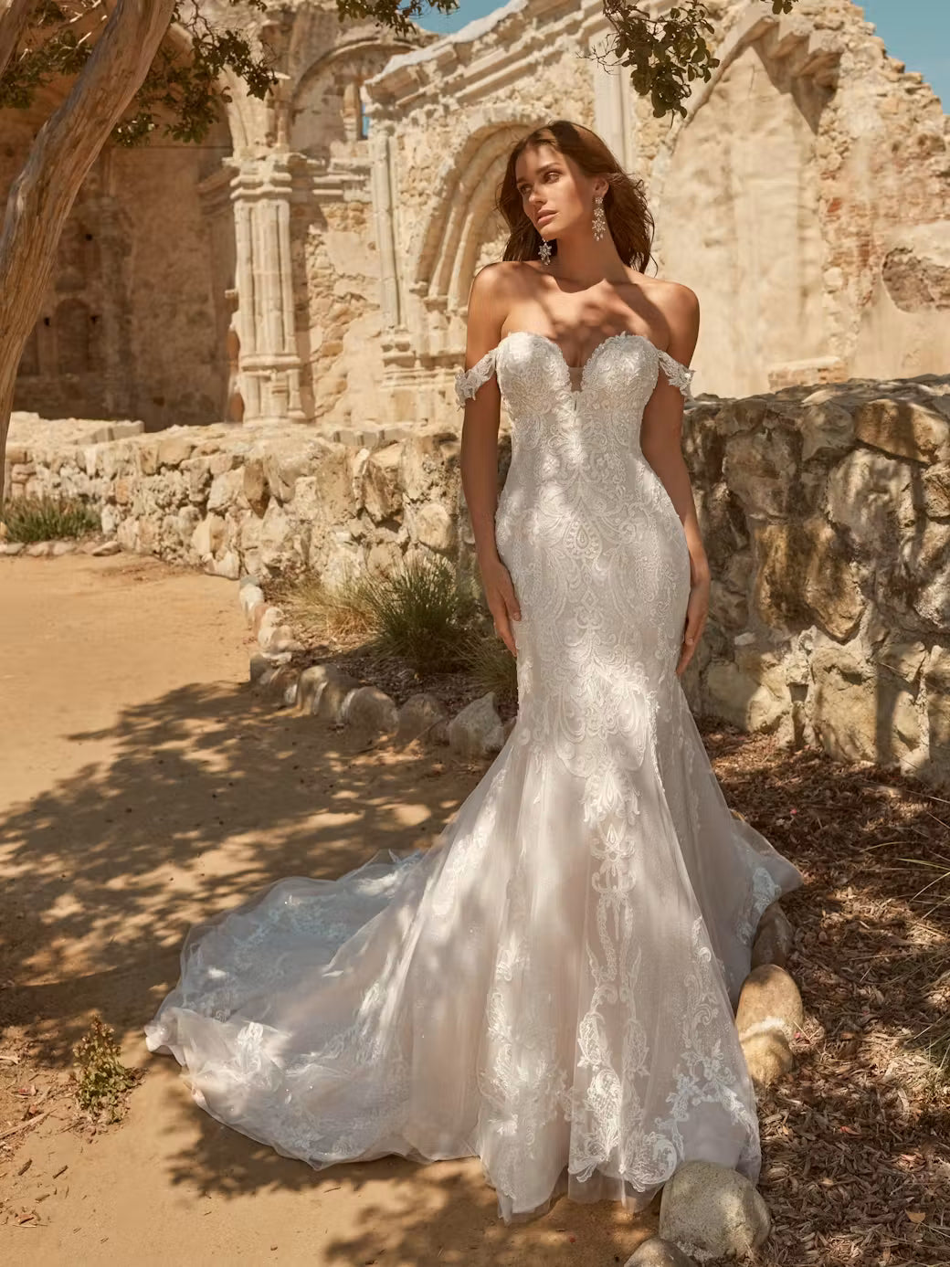 Woman in a white mermaid sweetheart plunging wedding dress, Frederique by Maggie Sottero, standing in front of stone ruins.