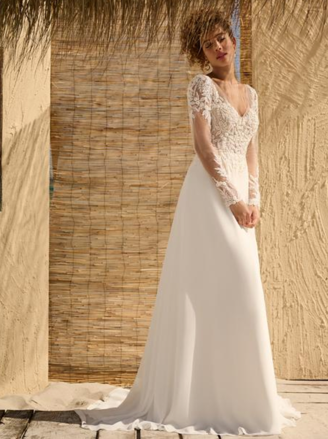 Woman in a white wedding dress with lace sleeves standing against a wooden backdrop