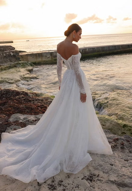 Woman in a white wedding dress standing on a beach at sunset.