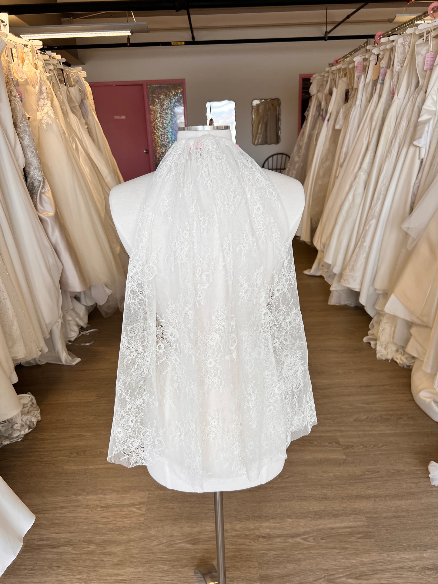 White lace wedding dress on a mannequin in a storage room with folded fabric.