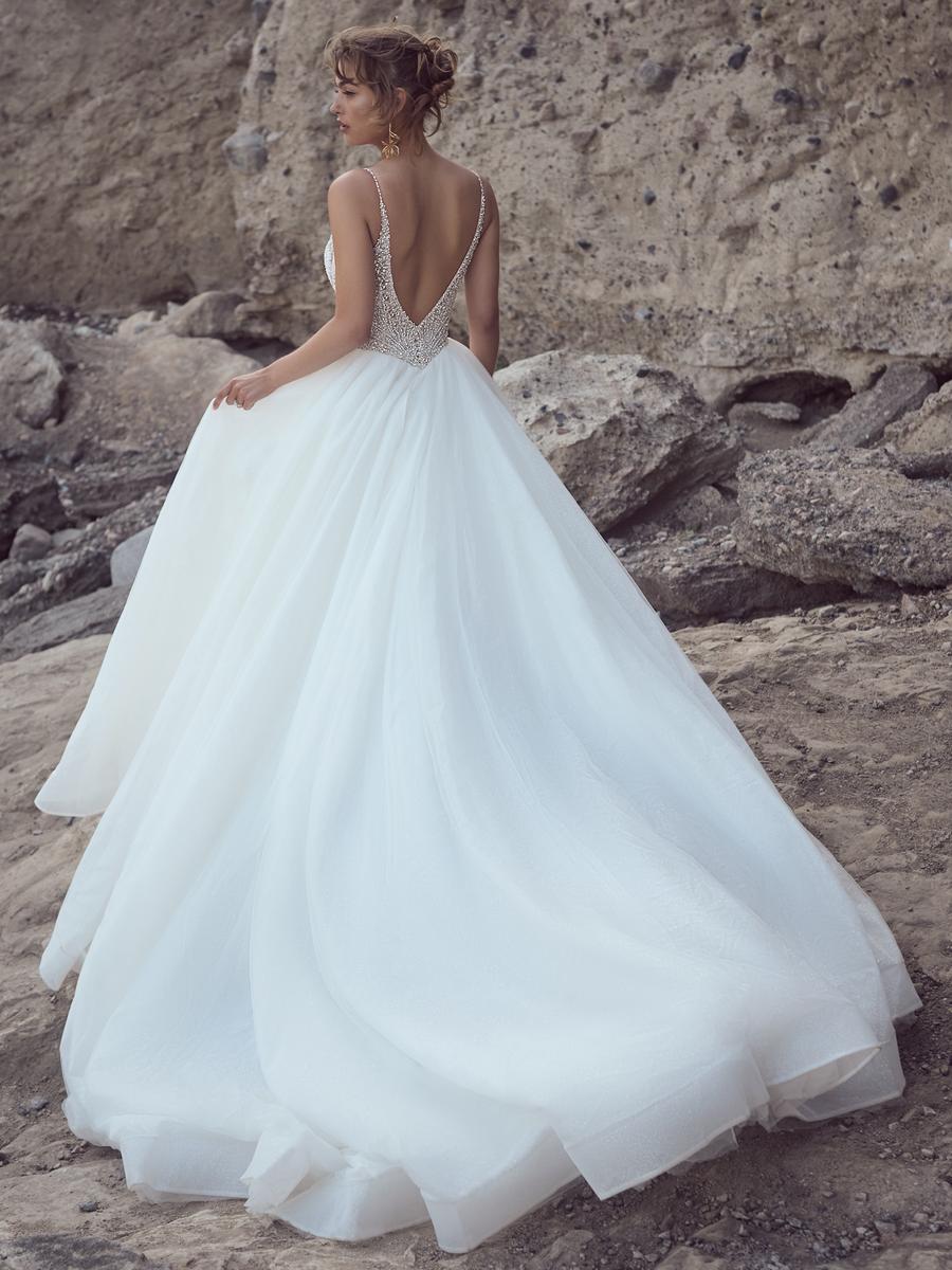 Woman in a white wedding dress with a open back standing on a rocky beach.