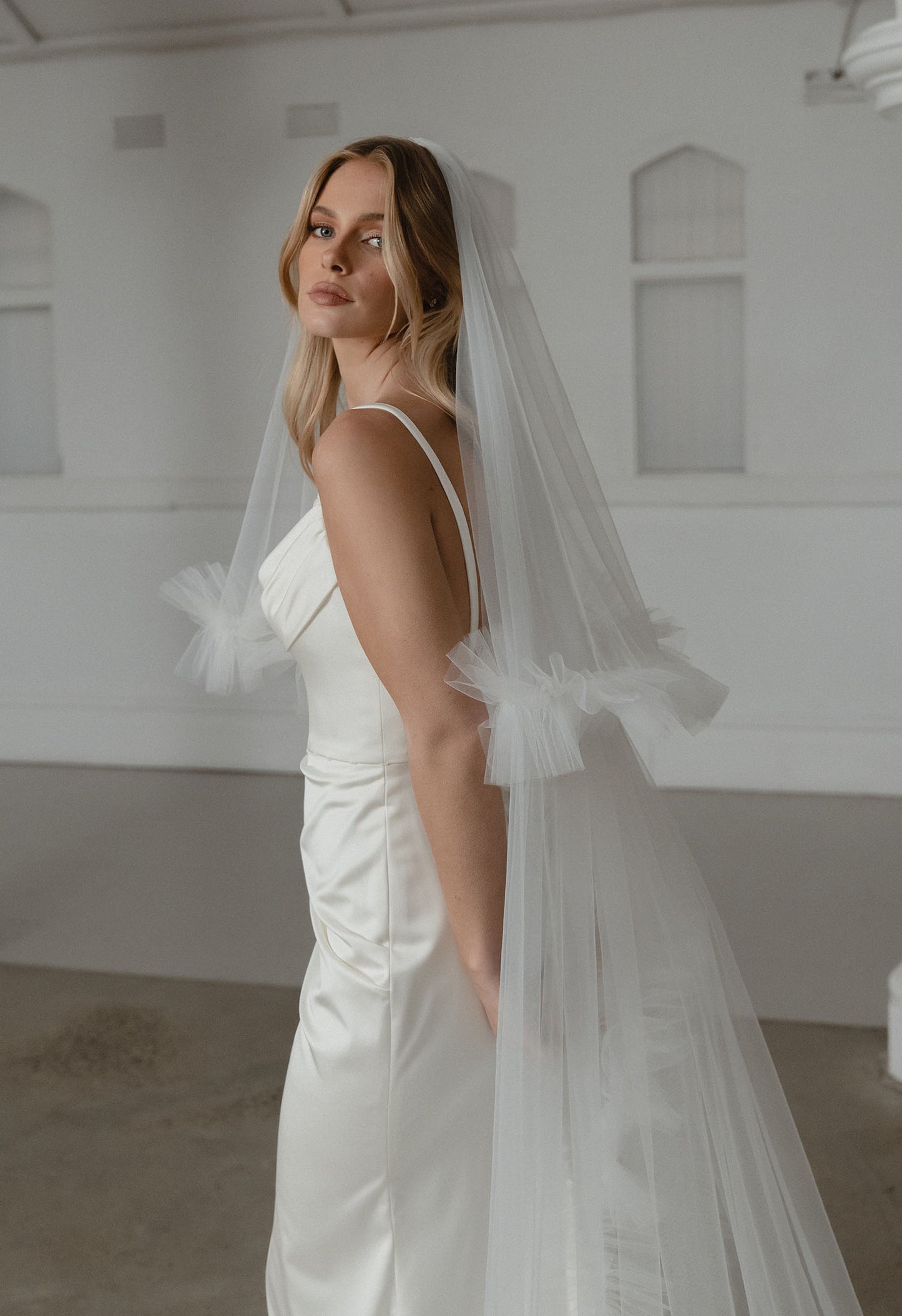 Woman wearing a white wedding dress with a veil in a minimalistic room.