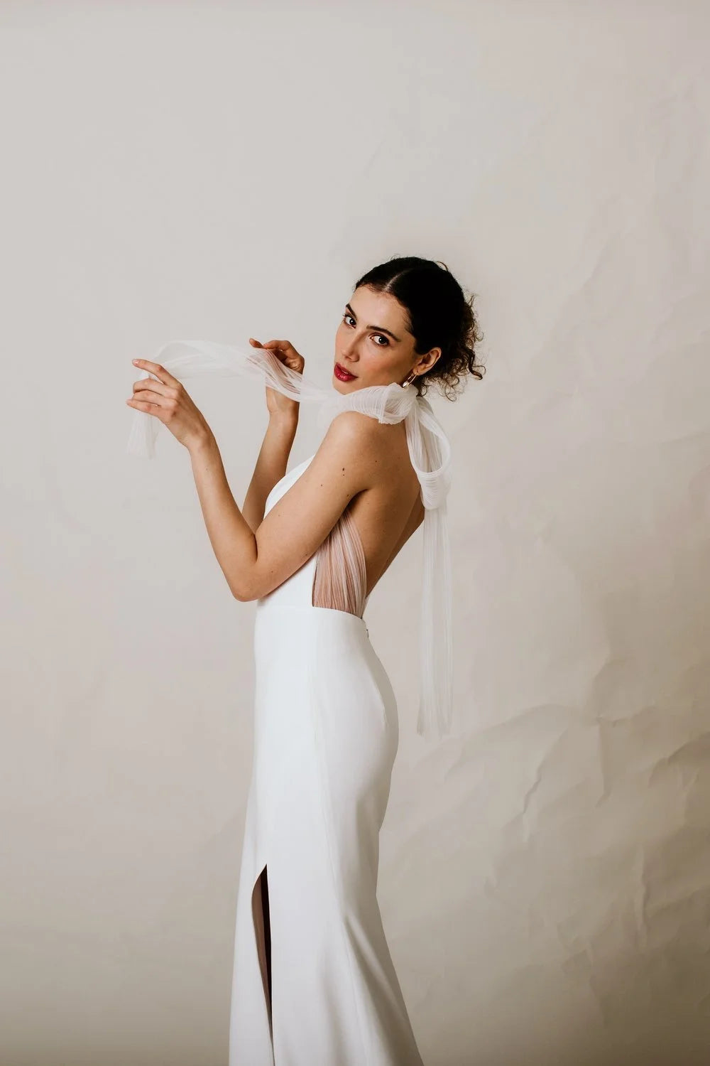 Woman wearing a white wedding dress with a sheer back against a plain background