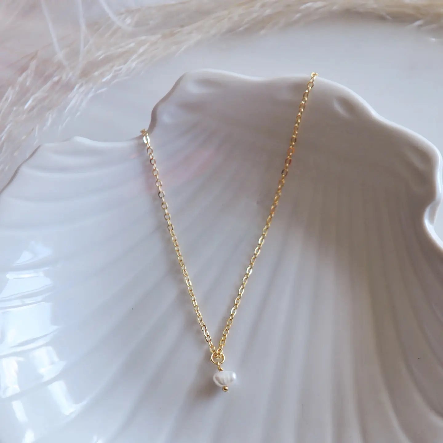 Gold pearl necklace with a dainty pearl on a shell bowl