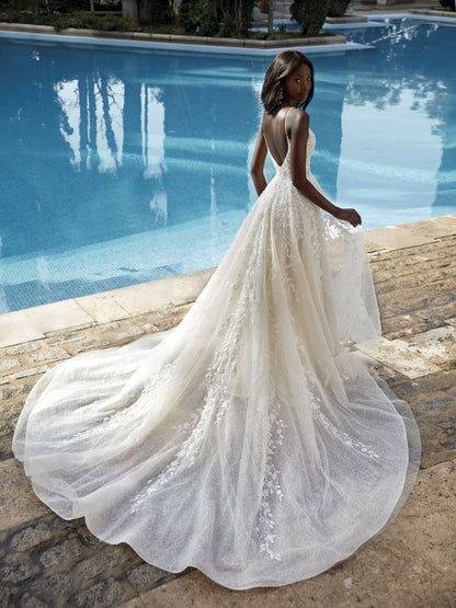 A woman showing off the low v-back of a sleeveless ivory wedding gown with floral lace embroidery and a full flowing skirt, 1199 by Demetrios. Style available at NKIN Bridal Ottawa