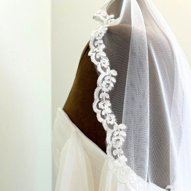 White wedding veil with lace trim on a mannequin against a white background