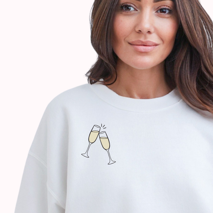 Woman wearing a white sweatshirt with champagne glass design on a plain background