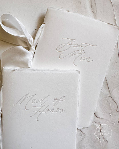 White vow book with silk ribbon and "maid of honor" pressed on the front and best man matching