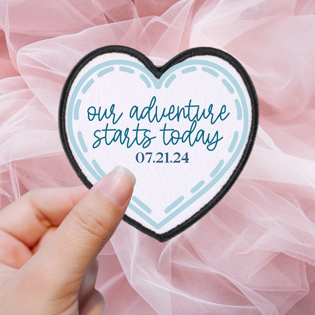 A white heart patch with "our adventure starts today 07.21.24" written in blue