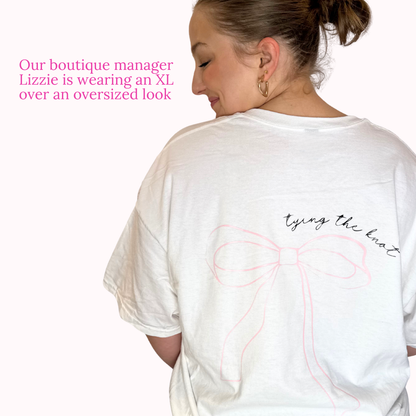 Person wearing a white oversized t-shirt with a bow design and text on a plain background