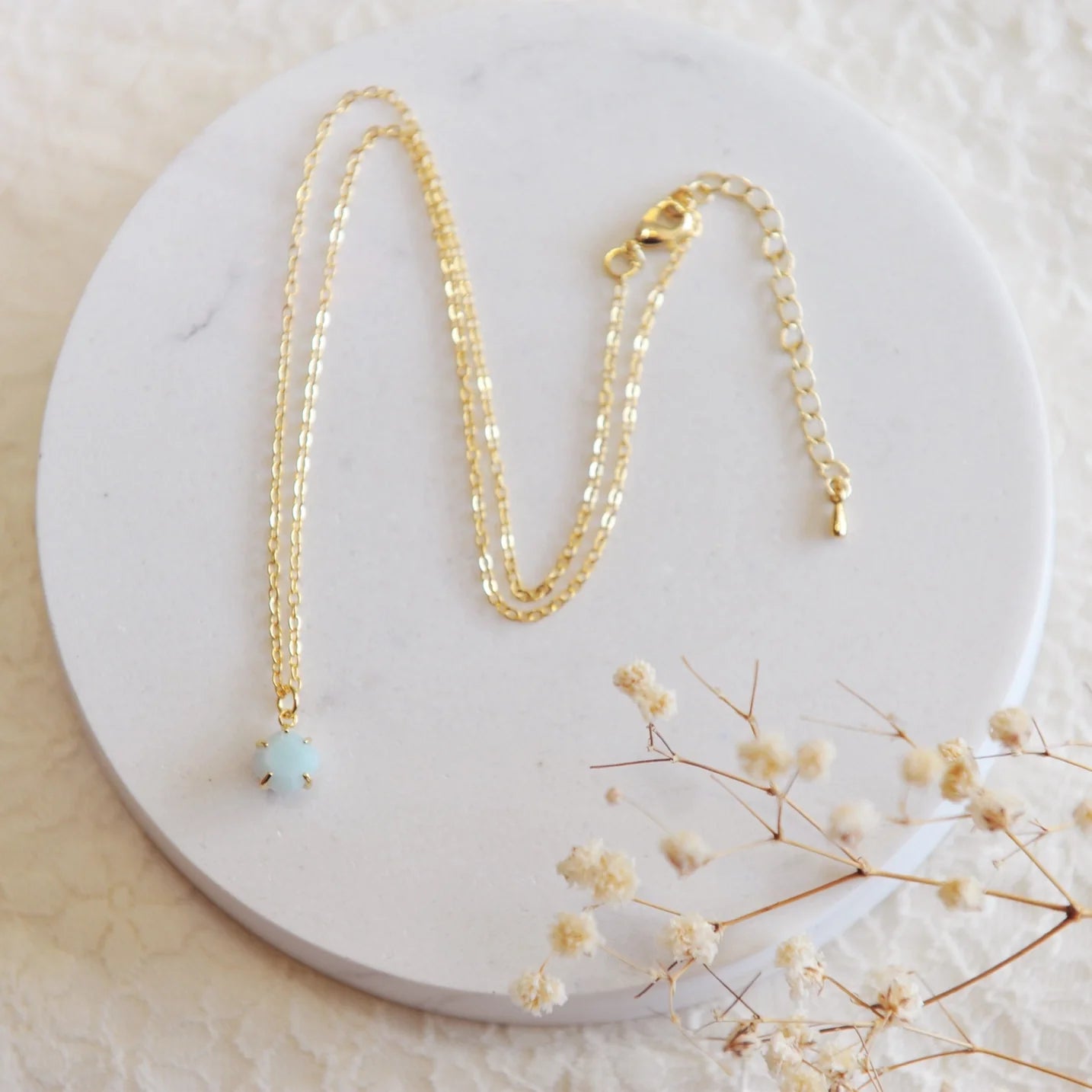 Gold necklace with a blue amazonite stone on a white stone backdrop