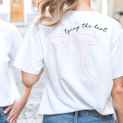 Person wearing a white t-shirt with a bow design and text outdoors