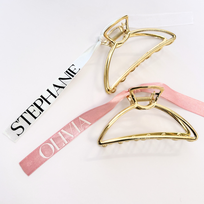 2 gold claw clips - One with a white ribbon that says "Stephanie" and one with a pink ribbon that says "Olivia"