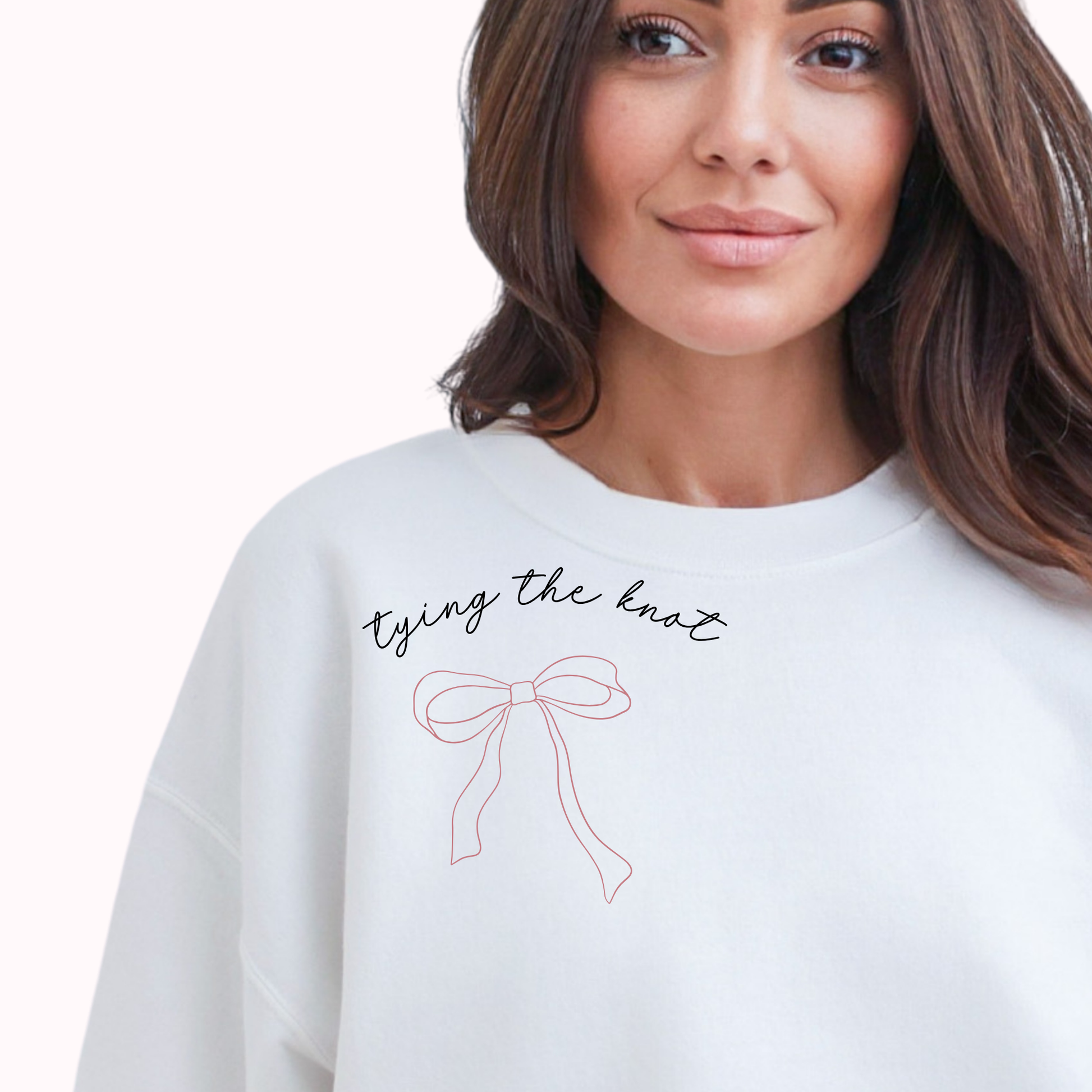 Woman wearing a white sweatshirt with 'tying the knot' text and bow design.