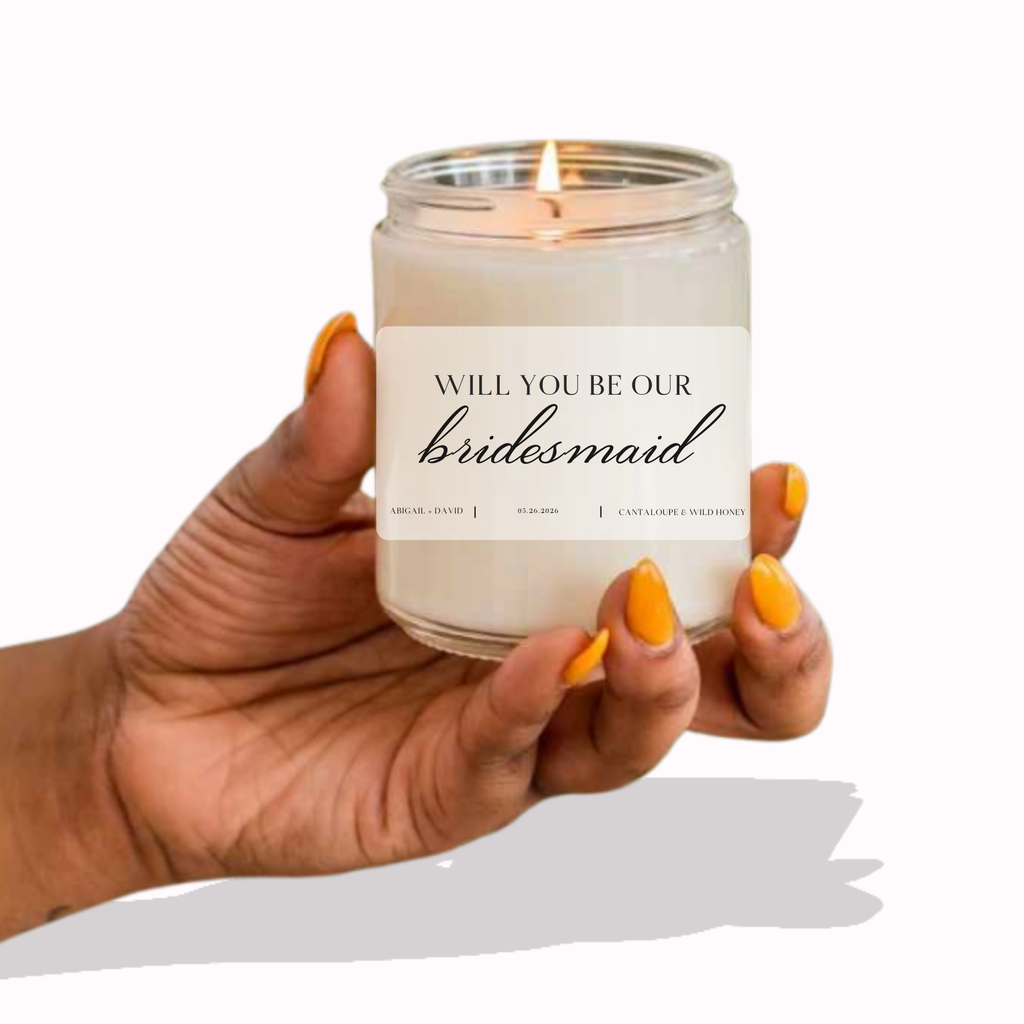 A candle with a label "will you be our bridesmaid" written on a white label with black text