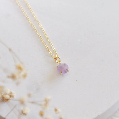 Gold necklace with a purple amethyst stone on a white stone backdrop