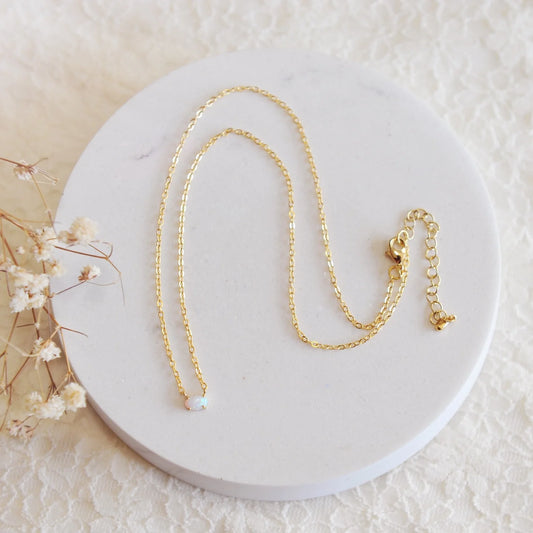 A white opal on a gold dainty chain on a white background
