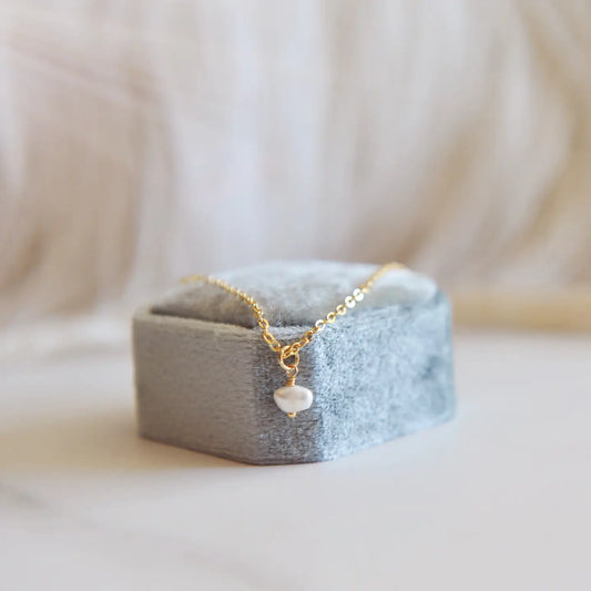 Gold pearl necklace with a dainty pearl on a grey ring box