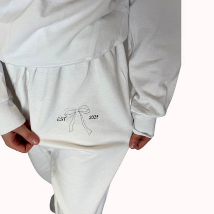 White outfit with a bow and 'EST 2025' text on a plain background
