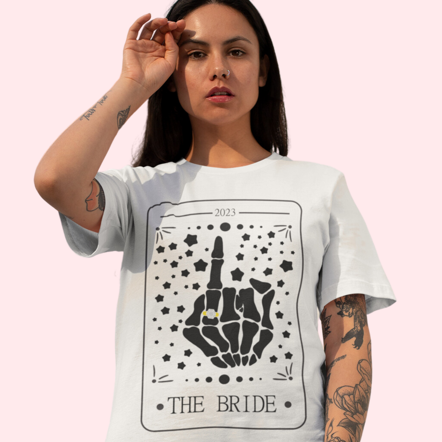 A young woman wearing a white shirt with "the bride" in a tarot card and a skeleton hand with a ring on the fourth finger.