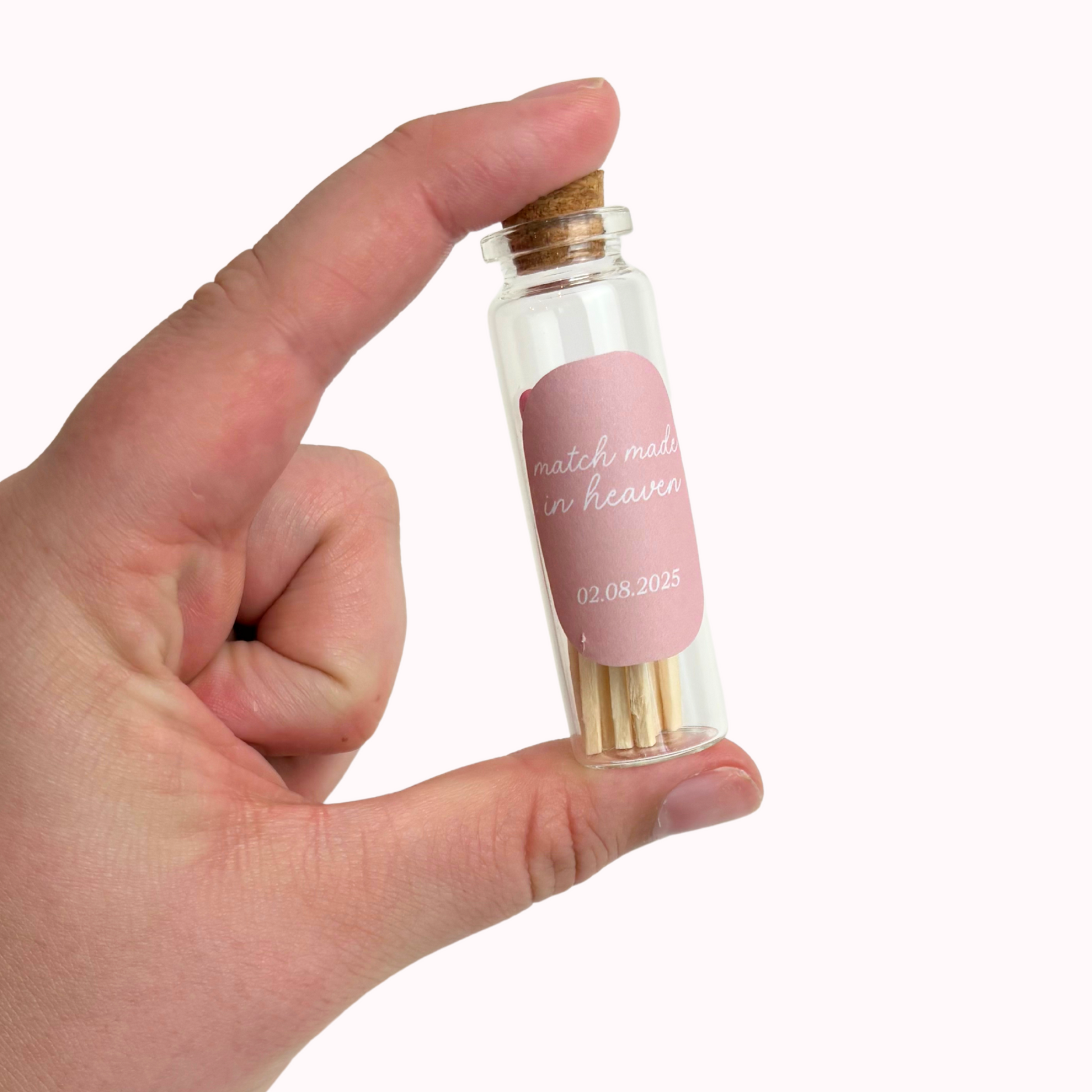 Hand holding a small glass bottle with a pink label and cork stopper.
