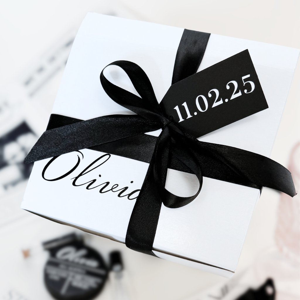 A white gift box with black ribbon, customized with "olivia" and a black gift tag with "11.02.25" written in white