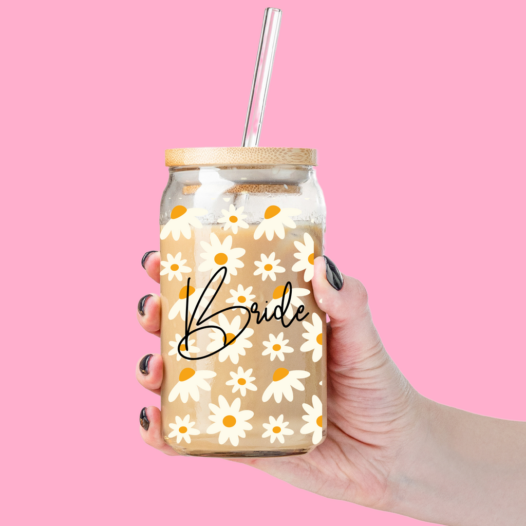 Glass tumbler with "Bride" written on it with daisy florals held by a hand.