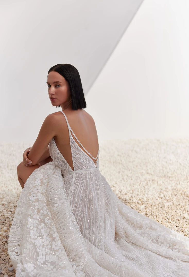 Woman in a white lace wedding dress sitting on a textured surface with a neutral background