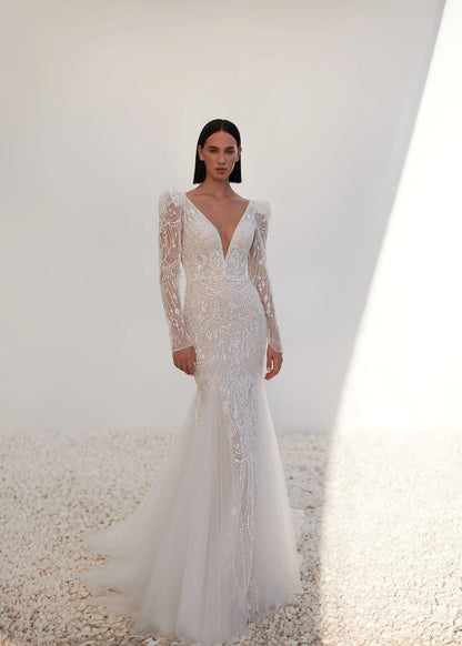 Model wearing a white wedding dress with long sleeves and a plunging neckline on a neutral background.