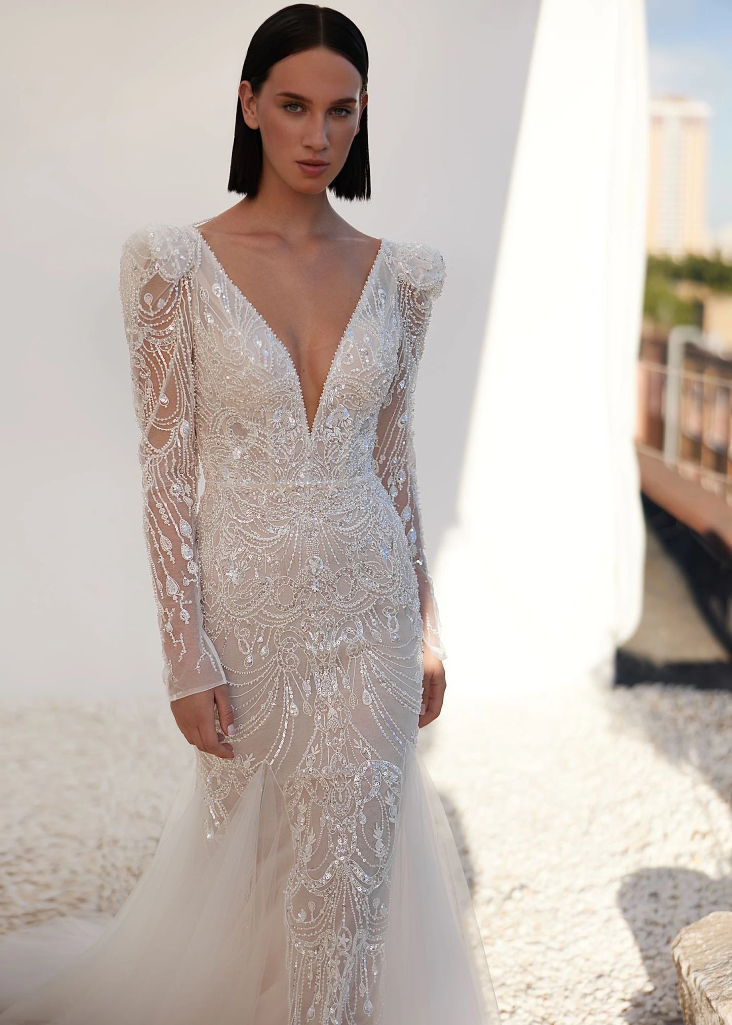 Woman wearing a white lace wedding dress with long sleeves against a blurred outdoor background.