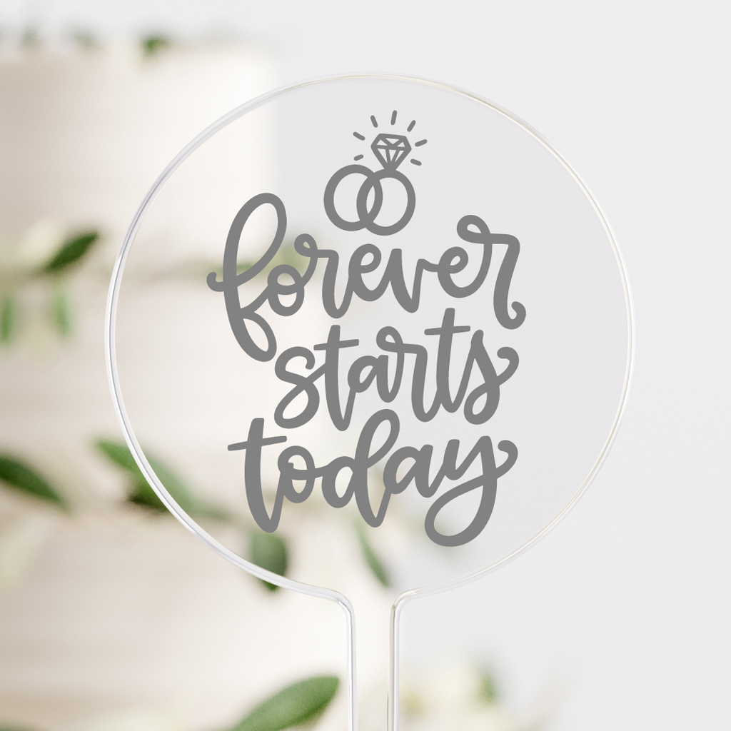 Circular clear cake topper with "forever starts today" written in silver