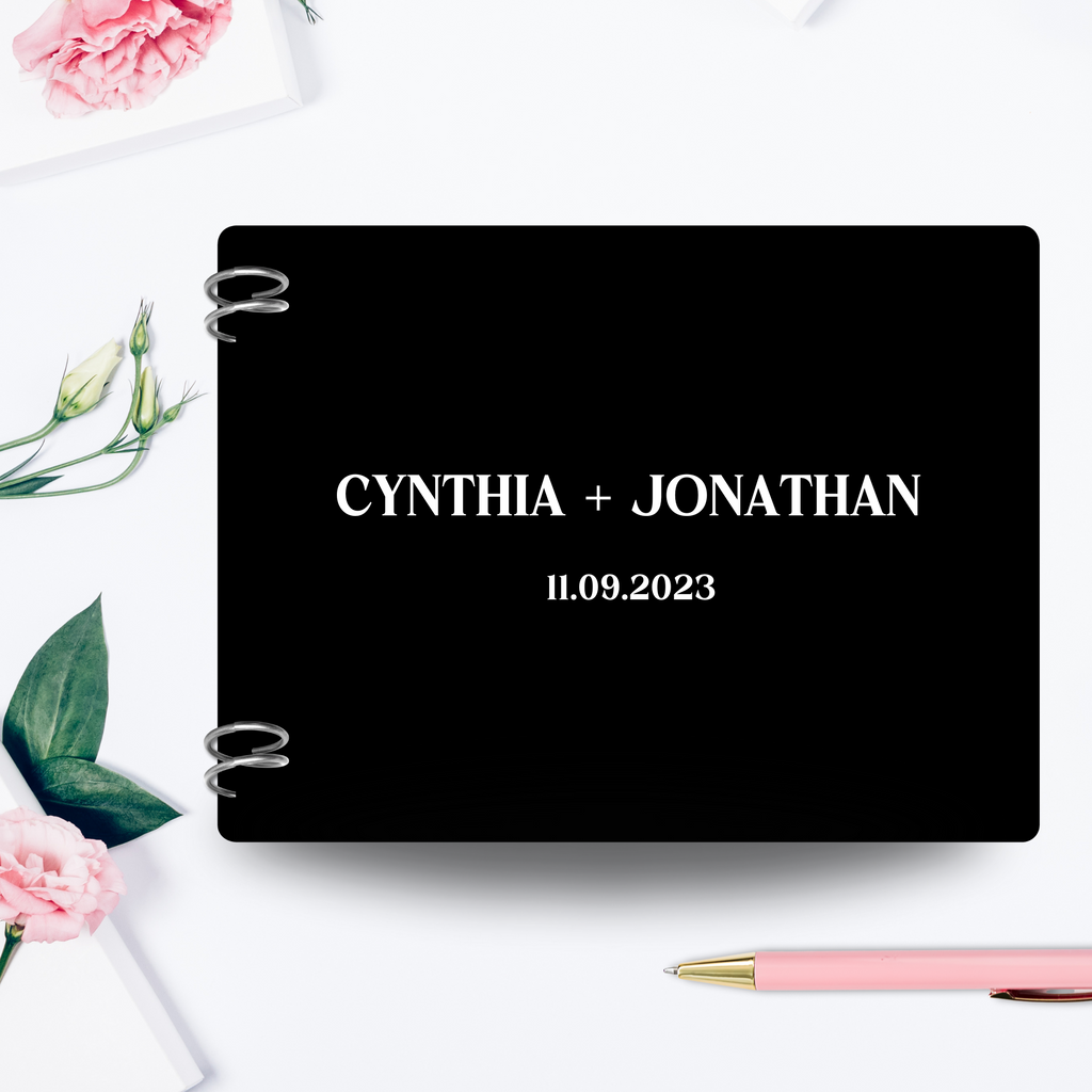 An acrylic black guest book with "Cynthia + Jonathan, 11.09.2023" printed in white vinyl