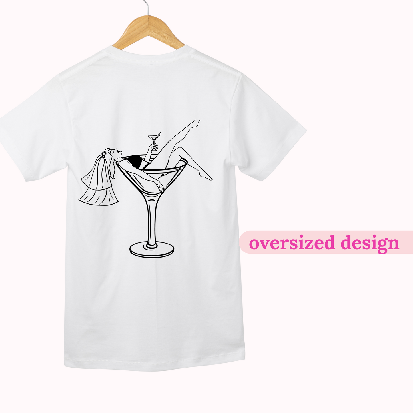 White t-shirt with a black graphic design of a martini glass and a person in a wedding dress, on a hanger with 'oversized design' text.