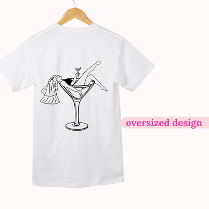 White t-shirt with a black graphic design of a martini glass and a person in a wedding dress, on a hanger with 'oversized design' text.