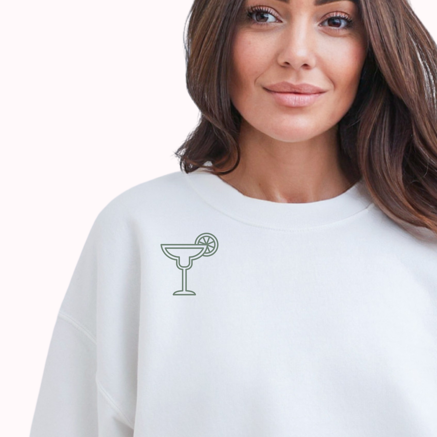 Woman wearing a white sweatshirt with a cocktail graphic on a plain background