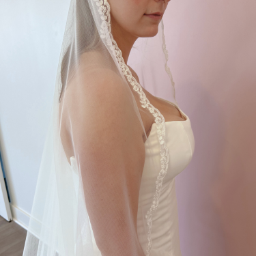 Woman wearing a white wedding dress and veil against a plain background