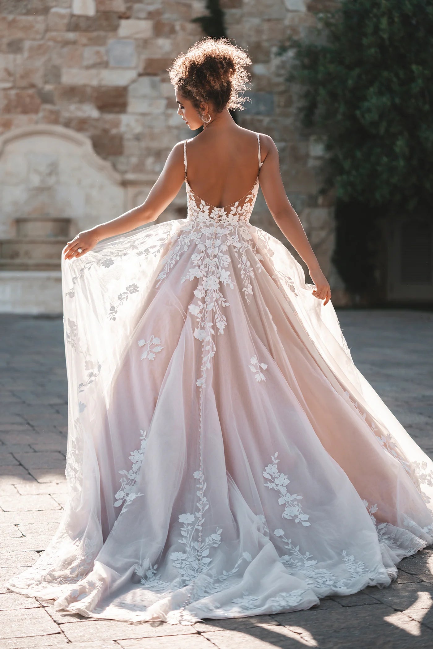 Woman in a pink wedding dress with floral details standing outdoors.