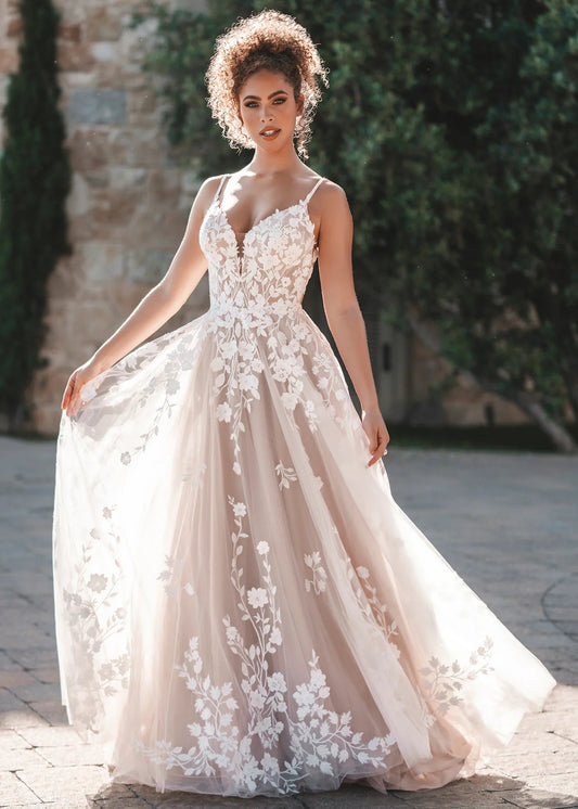 Woman in a floral wedding dress standing outdoors with greenery in the background
