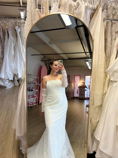 Abby taking a mirror selfie at NKIN, off the rack bridal shop, wearing a white strapless dress , the Elvira, in the NKIN showroom 