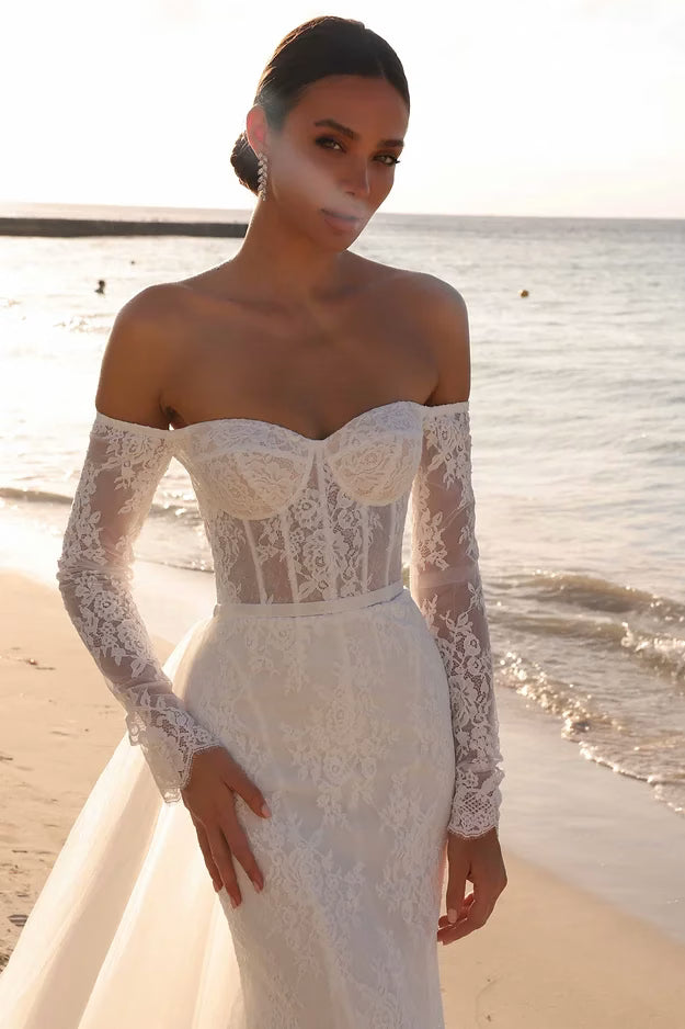 Woman in a white lace dress standing on a beach with ocean in the background