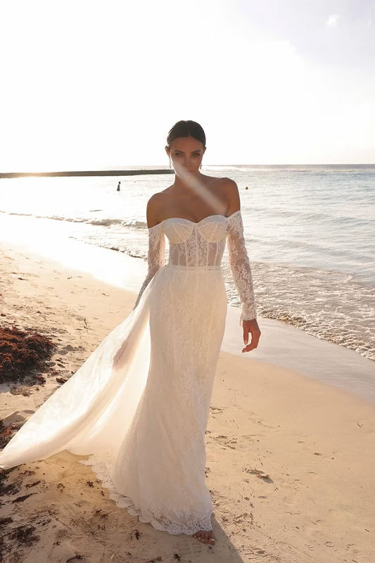 Woman in a white lace dress standing on a beach with ocean in the background