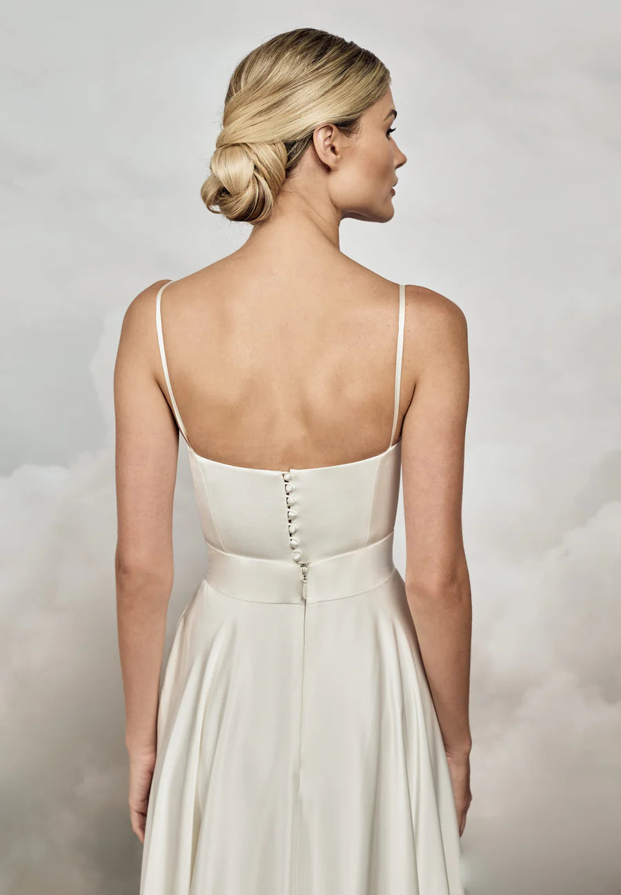 Woman wearing a white dress with thin straps against a soft, neutral background