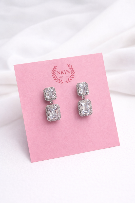 Pair of silver earrings on a pink card with 'NKIN' branding.