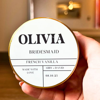 Round container labeled 'OLIVIA BRIDESMAID' held by a hand with a blurred background.